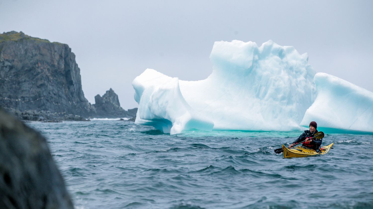 Kayaker with iceberg off Quirpon Island, Western