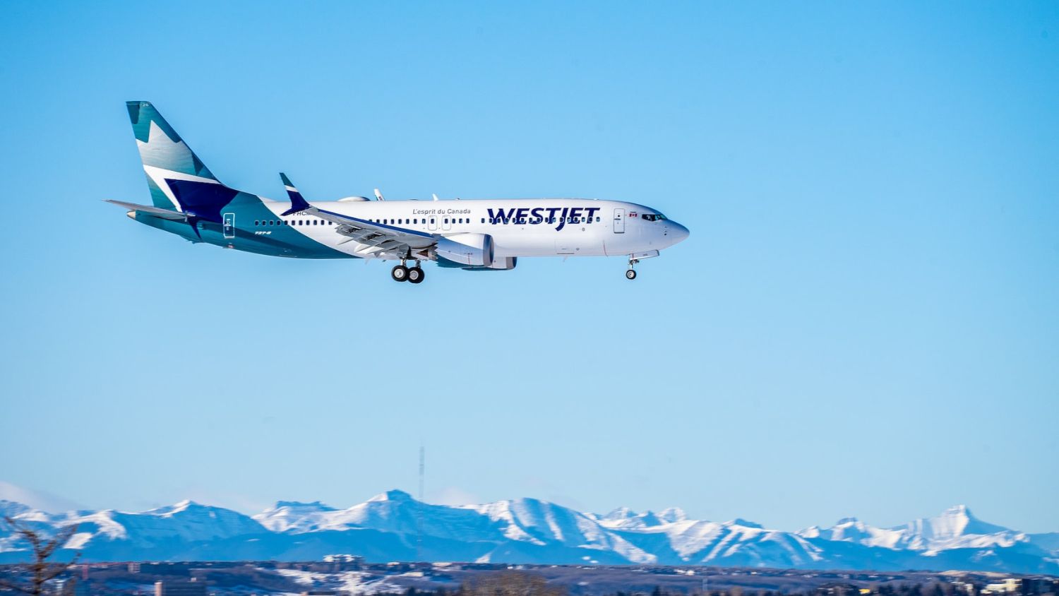WestJet Boeing 737 Max 8 arriving in Calgary against a beautiful mountain range.