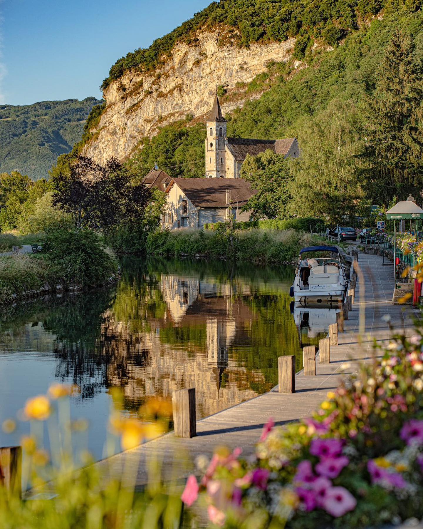 View of the Church of Chanaz seen from the Savières Canal, with surrounding greenery and calm water.
