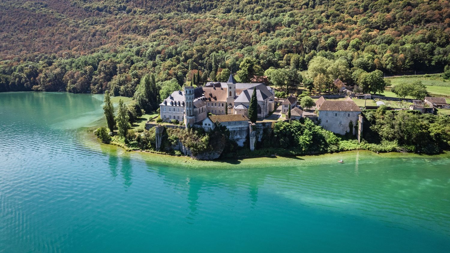 Aerial view of the historic Abbaye d’Hautecombe on the shores of Lake Bourget in Savoie, France, surrounded by water and greenery.