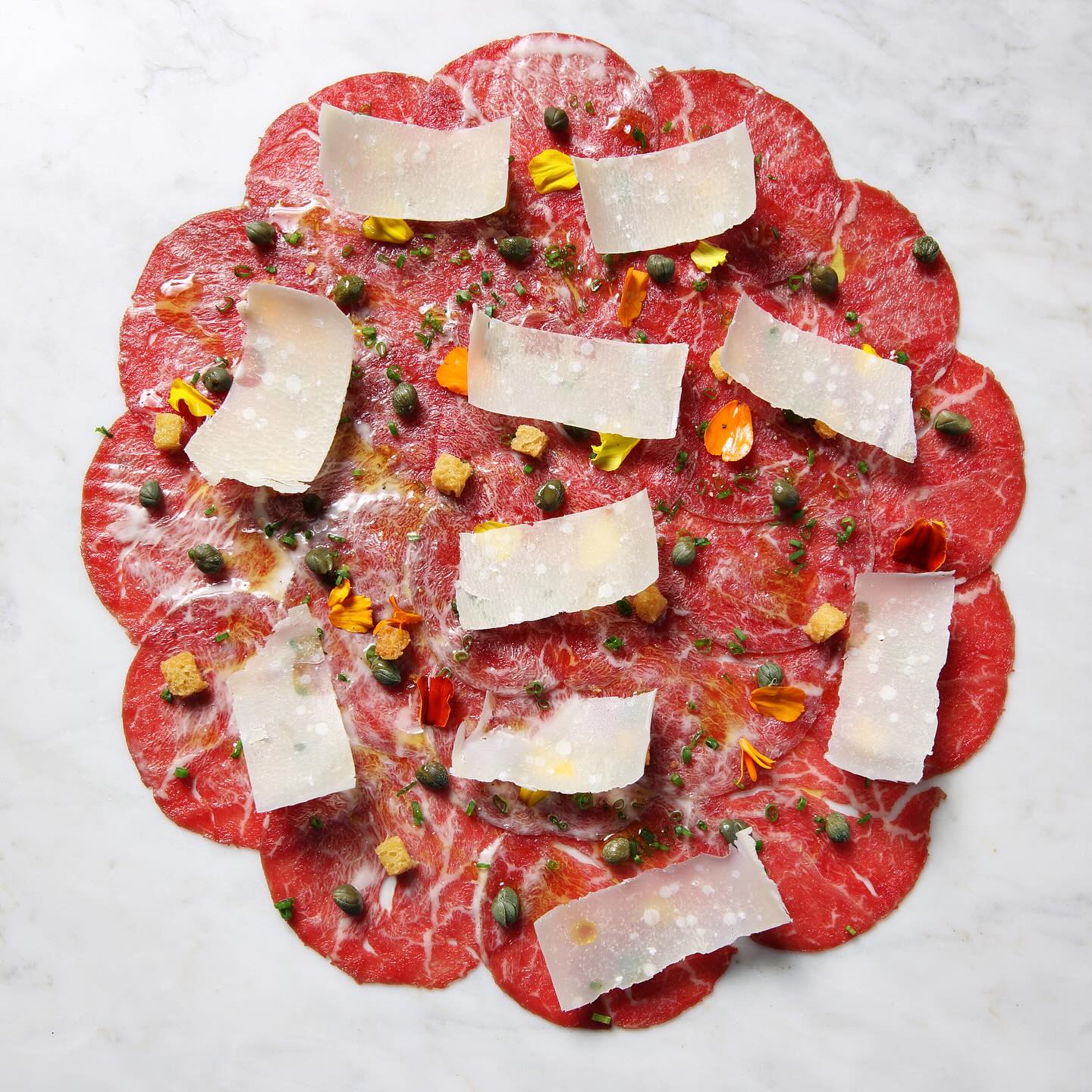 The Vittore 1950 Carpaccio: tenderloin of beef enhanced with black pepper, parmesan, capers, croutons, and sherry dressing—a true masterpiece for your palate.