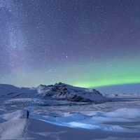 Glowing ribbons of green and purple shimmer over Fjallsárlón’s icy lagoon, reflecting off drifting icebergs beneath the towering Vatnajökull Glacier.