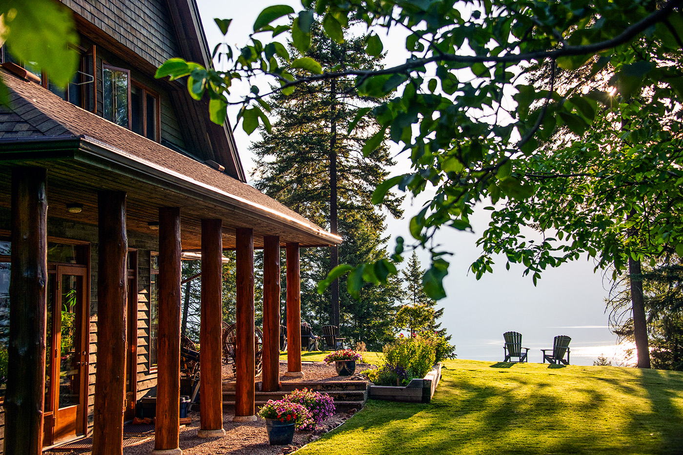 Scenic view of Mountain Trek Health Reset Retreat in Ainsworth, British Columbia, featuring the lodge, flower gardens and Adirondack chairs overlooking the water.