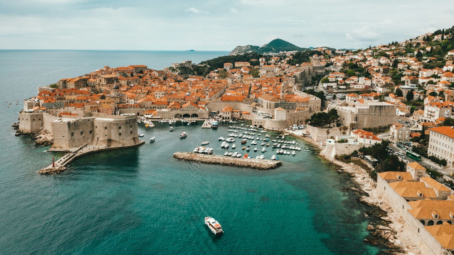 A view of Dubrovnik’s historic Old Town with medieval walls, terracotta rooftops, and stone palaces under a clear sky.