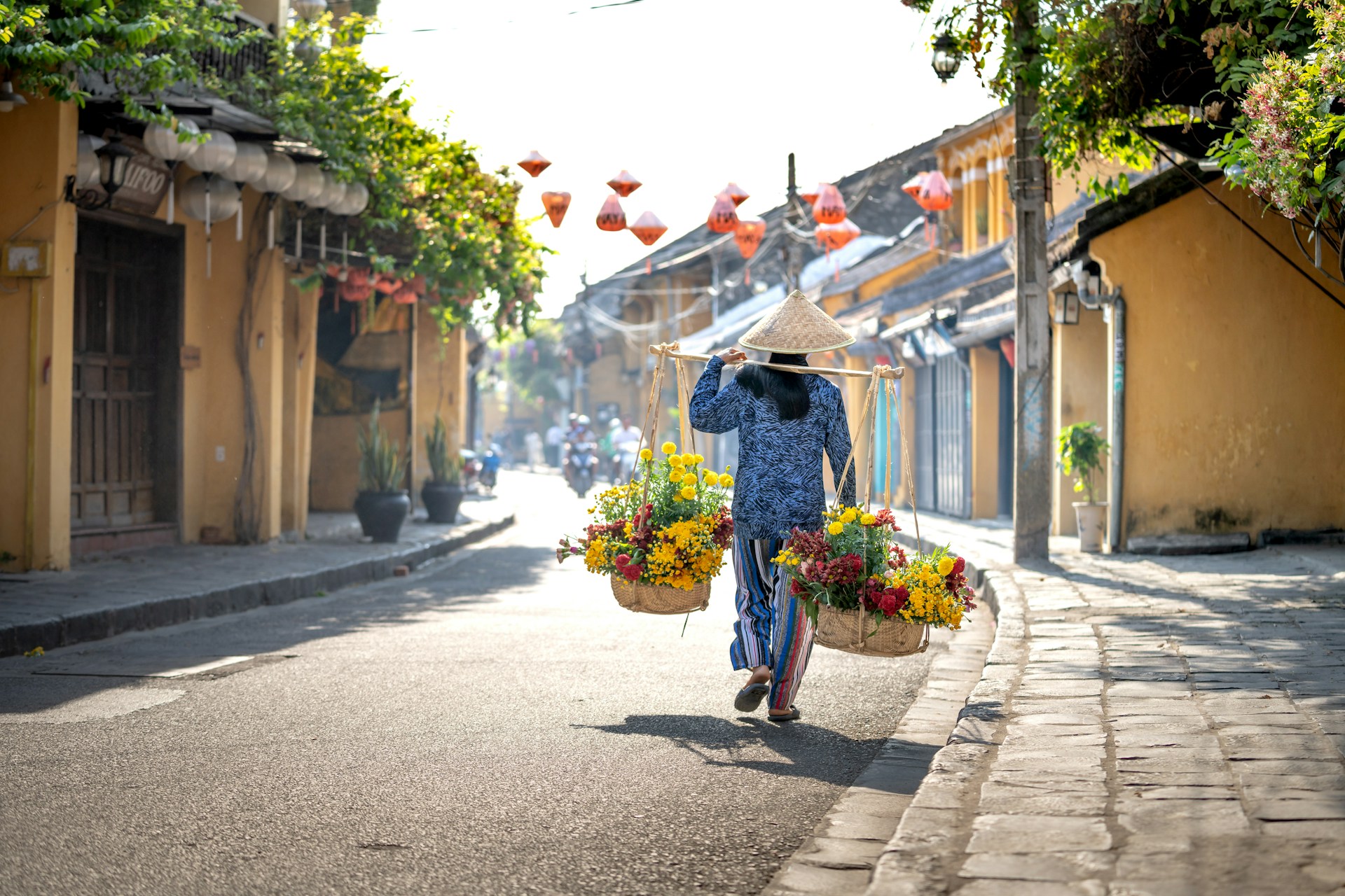 Flower vendor selling fresh blooms in Hoi An Ancient Town, Vietnam, with traditional Southeast Asian trading port architecture in the background.