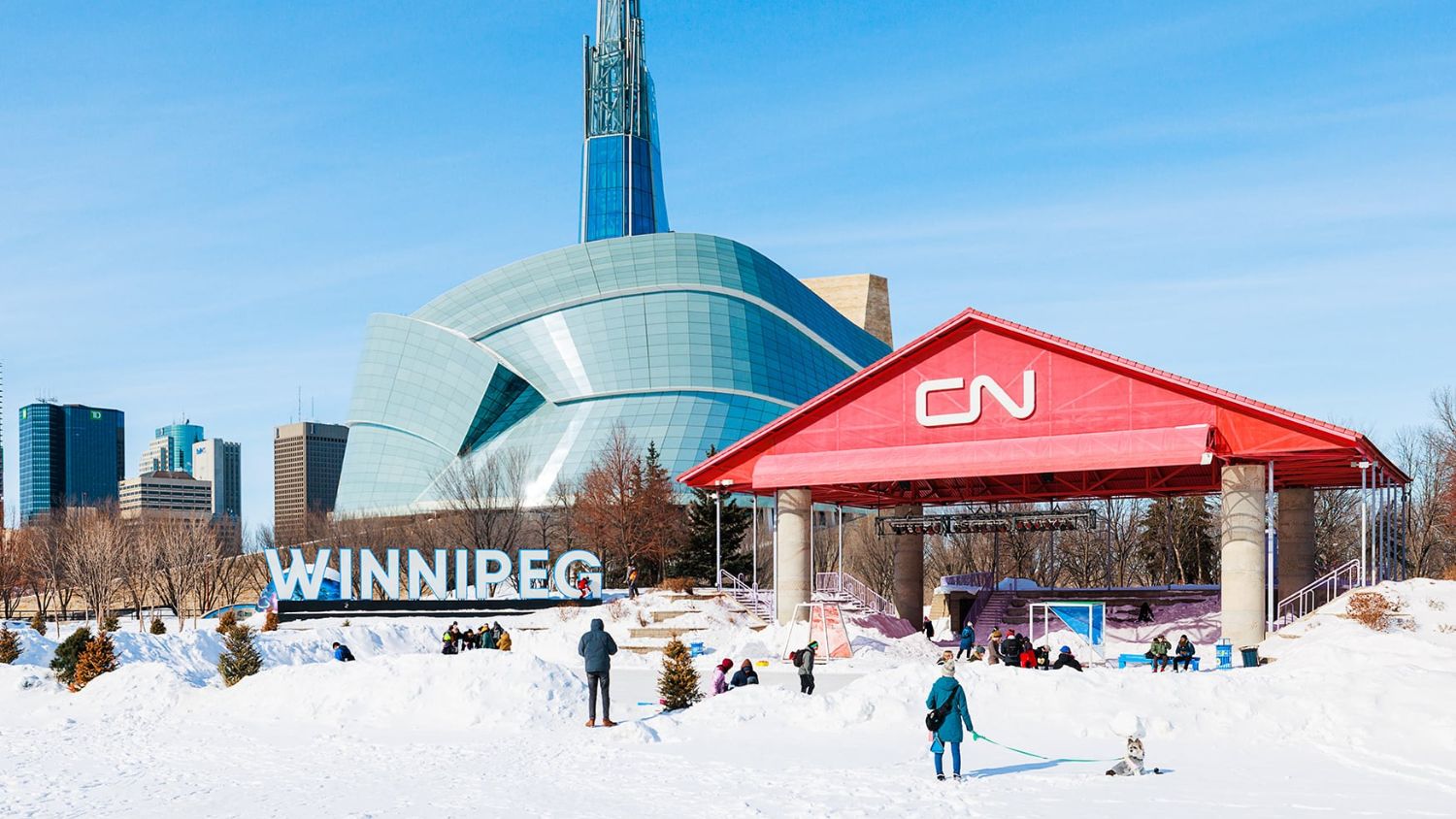 View of Winnipeg skyline from The Forks National Historic Site, showing rivers, historic buildings, and downtown cityscape.