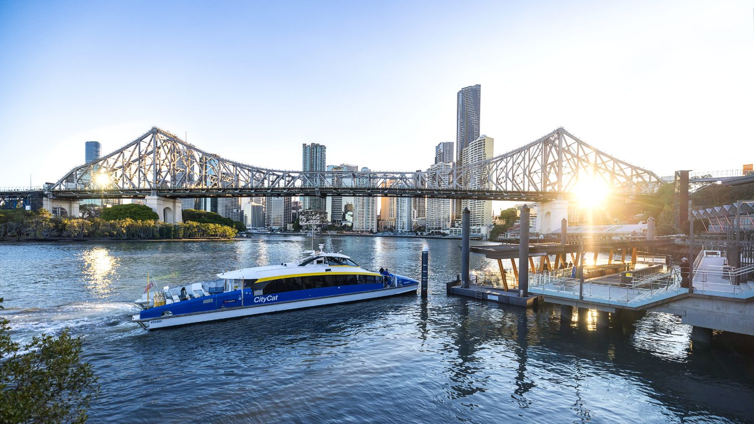 From the banks of the Brisbane River at Rivershed, the city skyline gleams in the warm afternoon light, with the iconic Story Bridge arching gracefully above